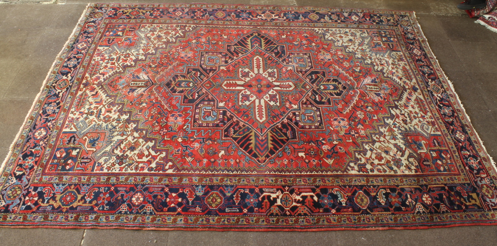 A Persian Heriz carpet with red white and blue ground and a stylised diamond medallion to the centre