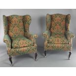 A pair of winged armchairs upholstered in green floral patterned material, raised on cabriole