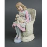 A 19th Century Continental bisque figure of a young girl sitting in a chair with a dog on her lap