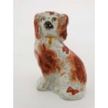 A Victorian Staffordshire spaniel decorated with iron red detail and ochre collar. Height 4”