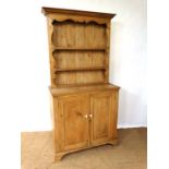 An early 20thC narrow pine dresser with open plate rack on a two door cupboard base with porcelain