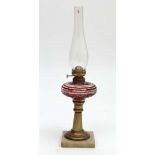 A late 19thC oil lamp with engraved and banded ruby glass reservoir on a brass columns and squared