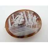 An oval cameo brooch depicting a classical scene of figures being chased from a classical