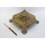A Victorian cast brass inkwell / Standish of squared form with relief decoration having hinged