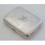 A silver cigarette case with hammered decoration, opening to reveal a gilded interior. Hallmarked