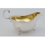 A silver sauce boat with scroll handle and 3 feet and gilded interior. Hallmarked Birmingham 1913