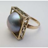 A 14ct gold dress ring set with a large pearl within a squared setting with scrolled frame