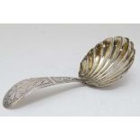 A white metal caddy spoon with engraved decoration to handle and scallop formed bowl. Indistinctly