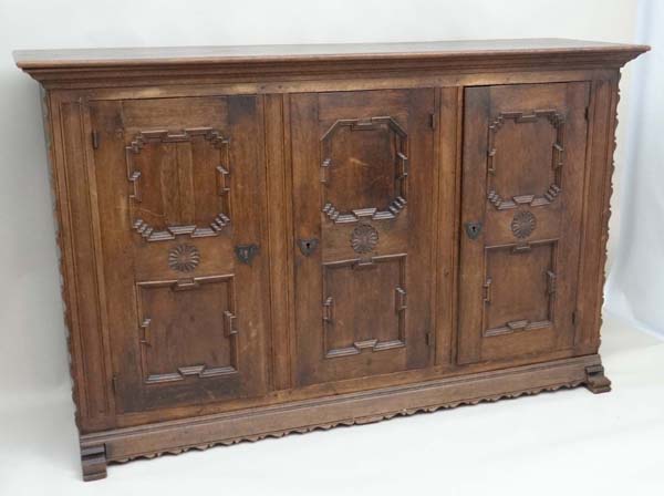 An early 20thC German oak 3 door cupboard with geometric like framed panelling, the doors opening to