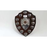 A wooden trophy shield with applied silver plate details. The centre with dartboard decoration. 10