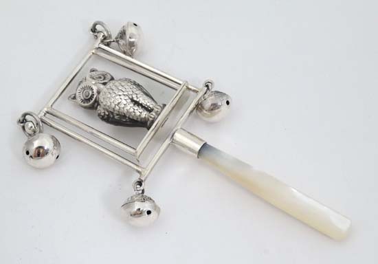 A white metal child's rattle decorated with owl and bells with mother of pearl teether handle.