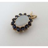 A yellow metal pendant set with central opal bordered by 12 sapphires 5/8" long CONDITION: Please