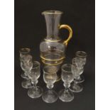 A clear glass jug on pedestal base with gilt detail and 7 matching liquer glasses. Jug 11 1/2'' high