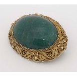 A white metal gilt brooch with large jade like cabochon to centre bordered by a scrolling filigree