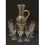 A clear glass jug on pedestal base with gilt detail and 7 matching liqueur glasses. Jug 11 1/2''