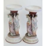 A matched pair of early 20thC bisque majolica style figural decorative urns, the urns each supported