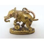 A gilt metal pendant fob seal formed as an elephant with red stone eyes and leg on a sphere.
