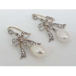 A pair of white metal drop earrings with pearl drops surmounted by bow detail set with white stones.