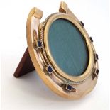 A small brass easel back photograph frame formed as a horseshoe with blue enamel style tops to nails