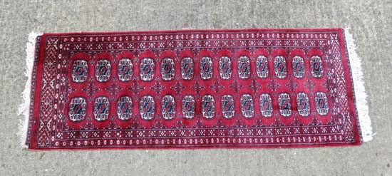 Rug / Carpet : a woollen Bokhara runner with 26 roundels to centre on a wine red back ground with