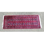 Rug / Carpet : a woollen Bokhara runner with 26 roundels to centre on a wine red back ground with