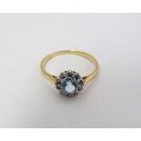 An 18ct gold ring set with central pale blue stone bordered by diamonds in a platinum setting.