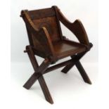 A late 19thC oak Glastonbury chair with carved decoration indistinctly marked verso and to arms 34