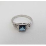 A silver ring set with central square topaz like blue stone flanked by chip set diamonds to