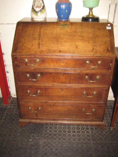 AN OAK BUREAU having a fall front enclosing an interior fitted with pigeon holes, drawers and