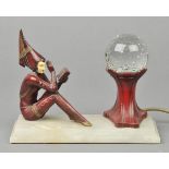 * Art Deco. A painted spelter table lamp in the form of a seated sorceress in the chryselephantine