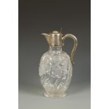 AN EDWARDIAN SILVER MOUNTED CLARET JUG with scroll handle and oval-shaped cut-glass body, on an oval