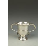 A GEORGE II TWO HANDLED CUP with flared rim and reeded girdle, with twin scrolling handles, on a