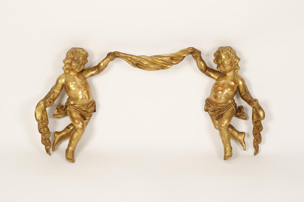 A ROCOCO STYLE CARVED GILTWOOD WALL MOUNT in the form of two figures amongst drapery, 32" wide