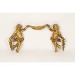 A ROCOCO STYLE CARVED GILTWOOD WALL MOUNT in the form of two figures amongst drapery, 32" wide