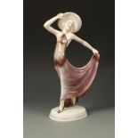 KATZHUTTE: A PORCELAIN MODEL OF AN ART DECO WOMAN wearing a hat and holding out her lilac dress,