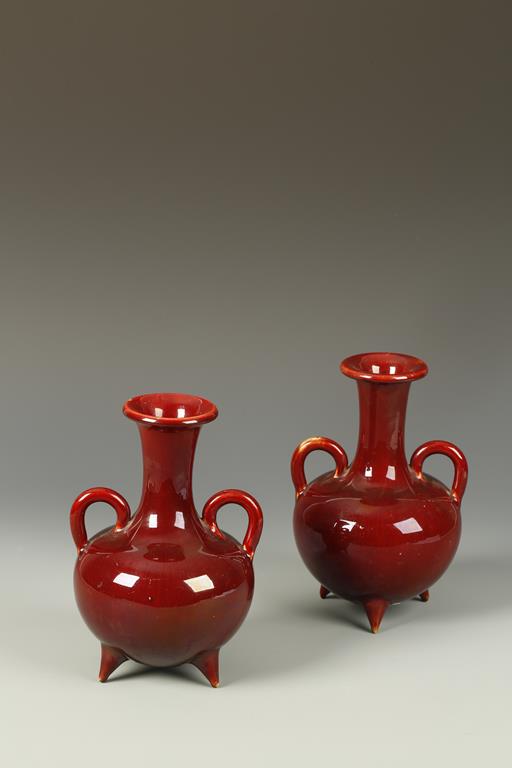 A PAIR OF RED GLAZE BOTTLE VASES with loop handles, on three tripod feet, possibly French Aesthetic,