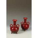 A PAIR OF RED GLAZE BOTTLE VASES with loop handles, on three tripod feet, possibly French Aesthetic,