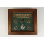 A COLLECTION OF NAZI BADGES, medal, and 'AFRIKA' cloth piece, displayed in glazed frame.