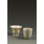 TWO CHINESE DEHUA CUPS, one of libation form with relief prunus decoration, the other decorated with