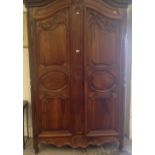 A large early 19th century French walnut armoire, with carved shaped doors and steel fittings on