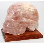 CARVED ROSE QUARTZ SKULL, H 6 1/2", L 8 1/2": Of typical form, with natural inclusions, on a wood