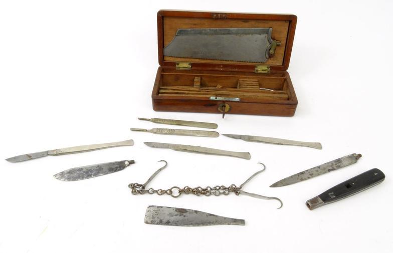 Selection of surgeon's tools including a saw, scalpel, knives and hooks, housed in a mahogany box,