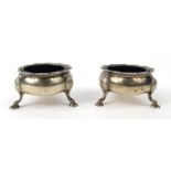 Pair of Georgian silver three footed salts with blue glass liners, indistinct London hallmarks,