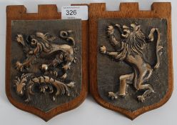 A pair of cast bronze armorial crests mounted to wooden plinths. Both with lion passants cast in