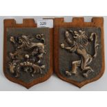 A pair of cast bronze armorial crests mounted to wooden plinths. Both with lion passants cast in