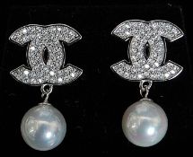 A pair of silver cultured pearl chanel style earrings. The interlinked C's inset with stones.