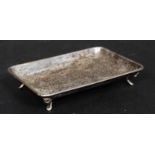 A hallmarked silver pin tray standing on four raised silver feet.