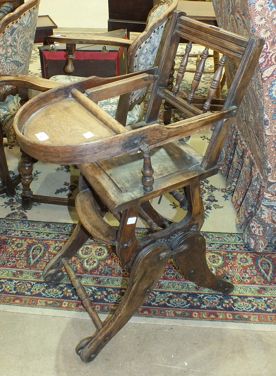 An Edwardian child's stained wood high chair on iron wheels.