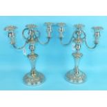 A pair of embossed decorated plated three-light candelabra on circular bases, 32cm high, (2).