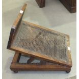 A Victorian stained wood and caned adjustable foot rest of double-hinged construction with label